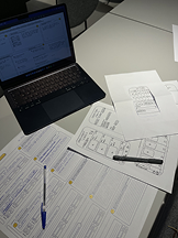 Usability testing setup: laptop running the prototype, printed task sheets and notes on the table
